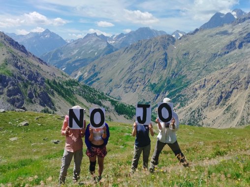 Photo de militantEs tenant des pancartes NO JO devant leurs visages avec, en fond, les Alpes